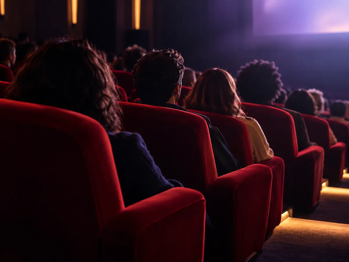 Fãs sentados em poltronas vermelhas de cinema assistindo à sessão